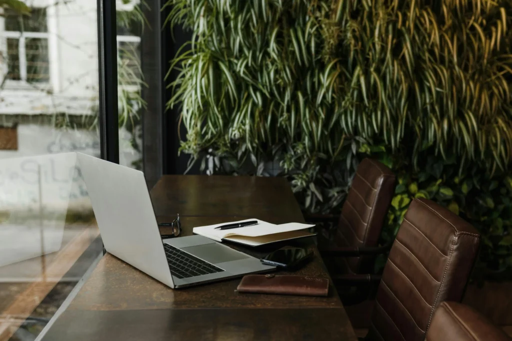 A sunlit classroom desk corner with an open blank notebook, pencil, stack of blank index cards, sticky notes, and small potted plant.