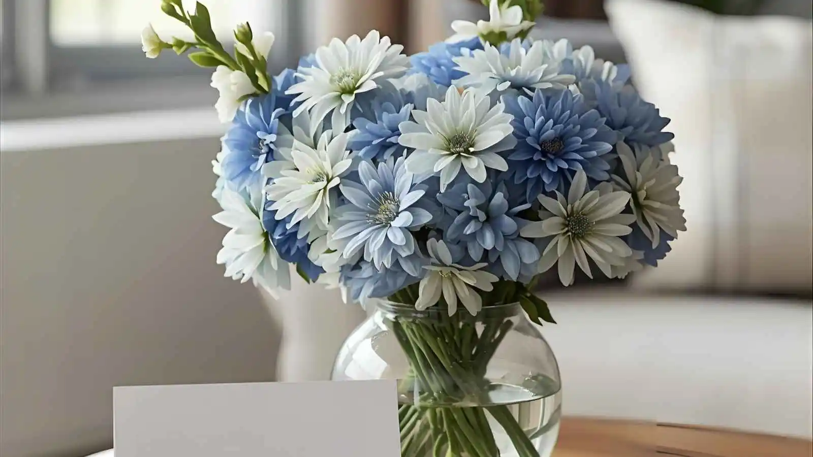 Blue-and-white flower bouquet in a glass vase with a blank greeting card on a table.